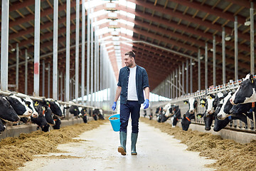 Image showing cows and man with bucket of hay walking at farm