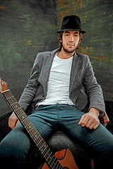 Image showing Cool guy sitting with guitar on gray background