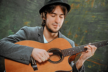 Image showing Cool guy with hat playing guitar on gray background