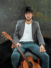 Image showing Cool guy sitting with guitar on gray background