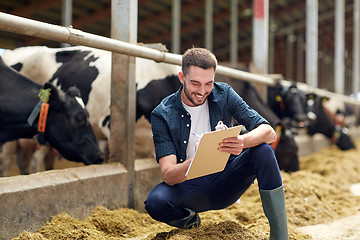 Image showing farmer with clipboard and cows in cowshed on farm