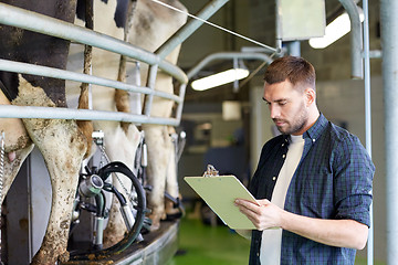 Image showing man with clipboard and milking cows on dairy farm