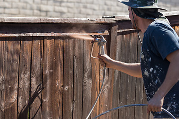 Image showing Professional Painter Spraying Yard Fence with Stain