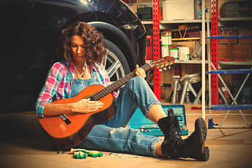 Image showing beautiful brunette car mechanic with a guitar sitting in a garag