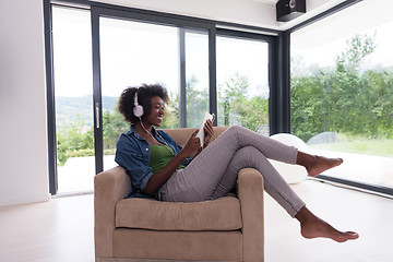 Image showing African american woman at home in chair with tablet and head pho