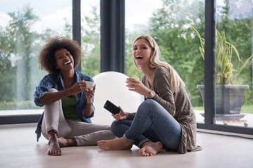 Image showing multiethnic women sit on the floor and drinking coffee