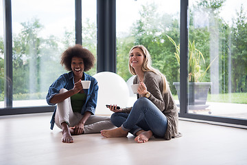 Image showing multiethnic women sit on the floor and drinking coffee