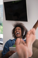 Image showing African american woman at home in chair with tablet and head pho