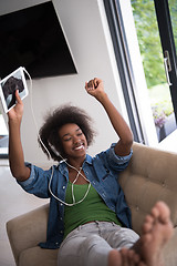 Image showing African american woman at home in chair with tablet and head pho