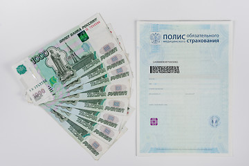 Image showing Next to the health insurance policy is a fan of thousand-pack of banknotes, white background