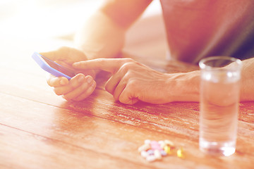 Image showing close up of hands with smartphone, pills and water