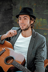 Image showing Cool guy sitting with guitar on gray background