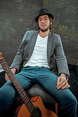 Image showing Cool guy sitting with guitar on gray background