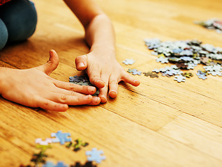 Image showing little kid playing with puzzles on wooden floor together with pa