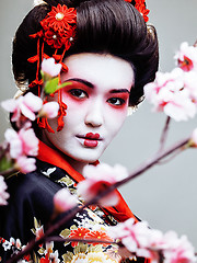 Image showing young pretty geisha in black kimono among sakura, asian ethno close up