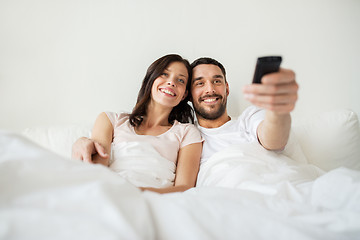 Image showing happy couple lying in bed at home and watching tv