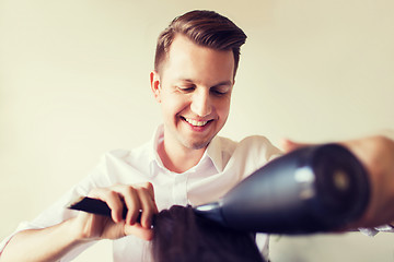 Image showing happy stylist with fan making blow-dry at salon