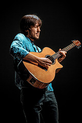 Image showing Cool guy standing with guitar on dark background