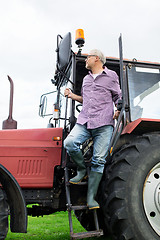 Image showing old man or farmer getting out of tractor at farm