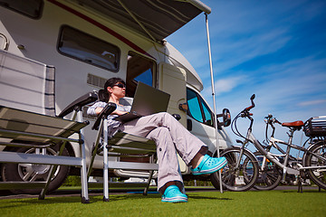 Image showing Woman sitting on a chair near the camper and looking at a laptop