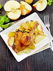 Image showing Duck leg with apple and basil in plate on dark board top