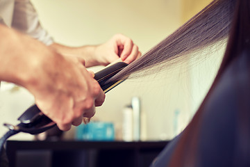 Image showing stylist with iron straightening hair at salon