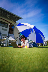 Image showing Woman on the grass, looking at the laptop under umbrella near th