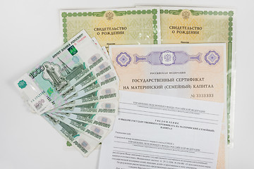 Image showing On a white background are two of a birth certificate, a certificate for maternity capital, receipt of a notice of a certificate and a packet of money