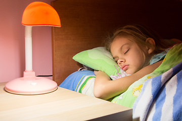 Image showing Seven-year girl asleep in bed, reading lamp is included on the next table