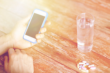 Image showing close up of hands with smartphone, pills and water