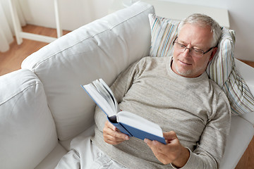 Image showing senior man lying on sofa and reading book at home