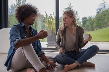 Image showing multiethnic women sit on the floor and drinking coffee