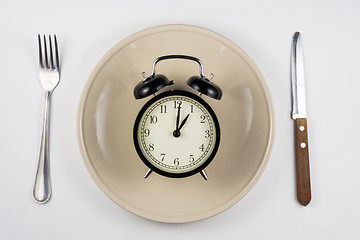 Image showing On the plate is an alarm clock, lying next to a knife and fork, white background, top view