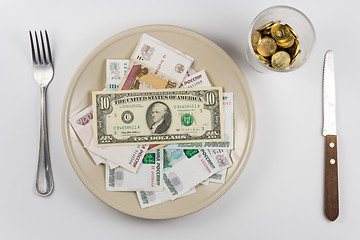 Image showing On the plate is a lot of money Russian ruble and the US dollar, standing next to a glass and a fork and knife lie, top view