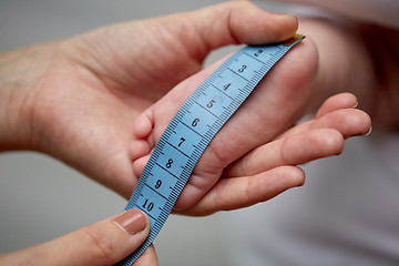 Image showing close up of hands with tape measuring baby foot