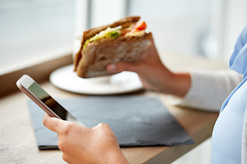 Image showing woman with smartphone and sandwich at restaurant