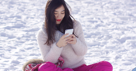 Image showing Young woman sat on snow texting on mobile