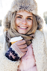 Image showing young pretty teenage hipster girl outdoor in winter snow park having fun drinking coffee, warming up happy smiling, lifestyle people concept