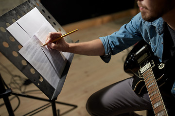 Image showing man with guitar writing to music book at studio