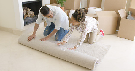 Image showing Young couple rolling up a rug as they move house