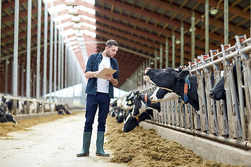 Image showing farmer with clipboard and cows in cowshed on farm