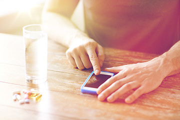 Image showing close up of hands with smartphone, pills and water