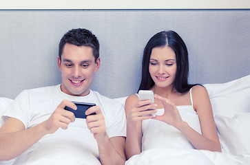 Image showing smiling couple in bed with smartphones