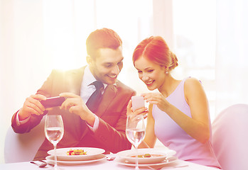 Image showing smiling couple with appetizers and smartphones