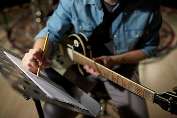 Image showing man with guitar writing to music book at studio