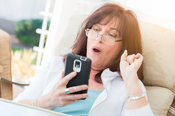 Image showing Shocked Middle Aged Woman Gasps While Using Her Smart Phone