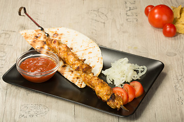 Image showing shashlik. kebab skewer, black rectangular plate. sauce and onions