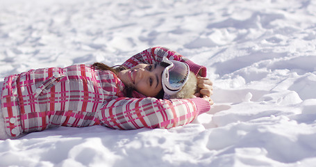 Image showing Young woman lying on snow with ski goggles