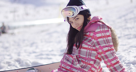 Image showing Beautiful asian snowboarder sitting on snow