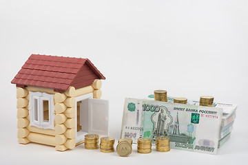 Image showing At toy house opened the door, the door are stacks of coins and bundles of bank notes, coins in the foreground with the word \